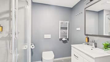 Un baño moderno con cabina de ducha de vidrio, inodoro blanco, toallero y lavamanos con espejo.