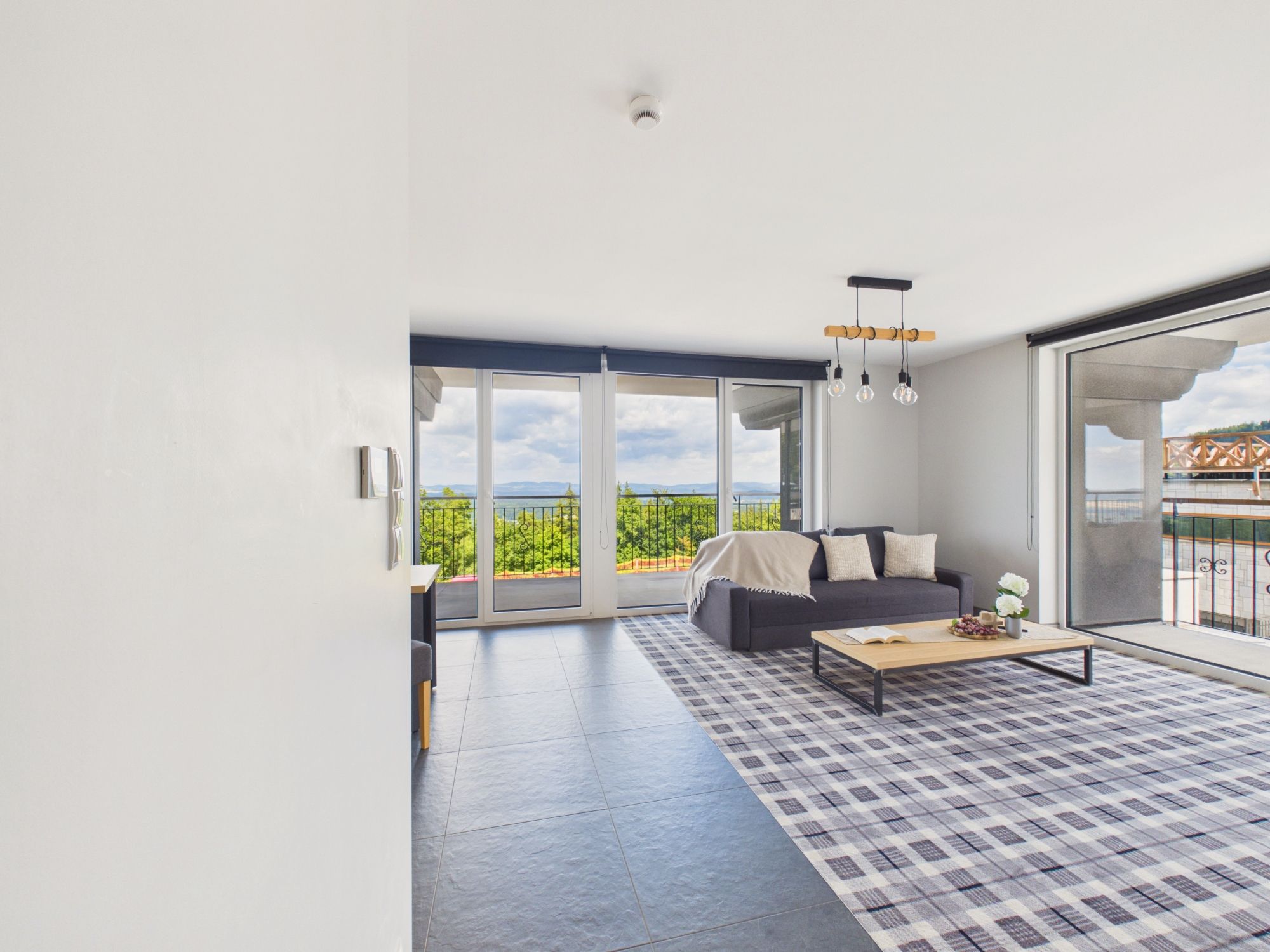 Una sala de estar moderna con un sofá, una mesa de centro y ventanas amplias con vistas a zonas verdes.