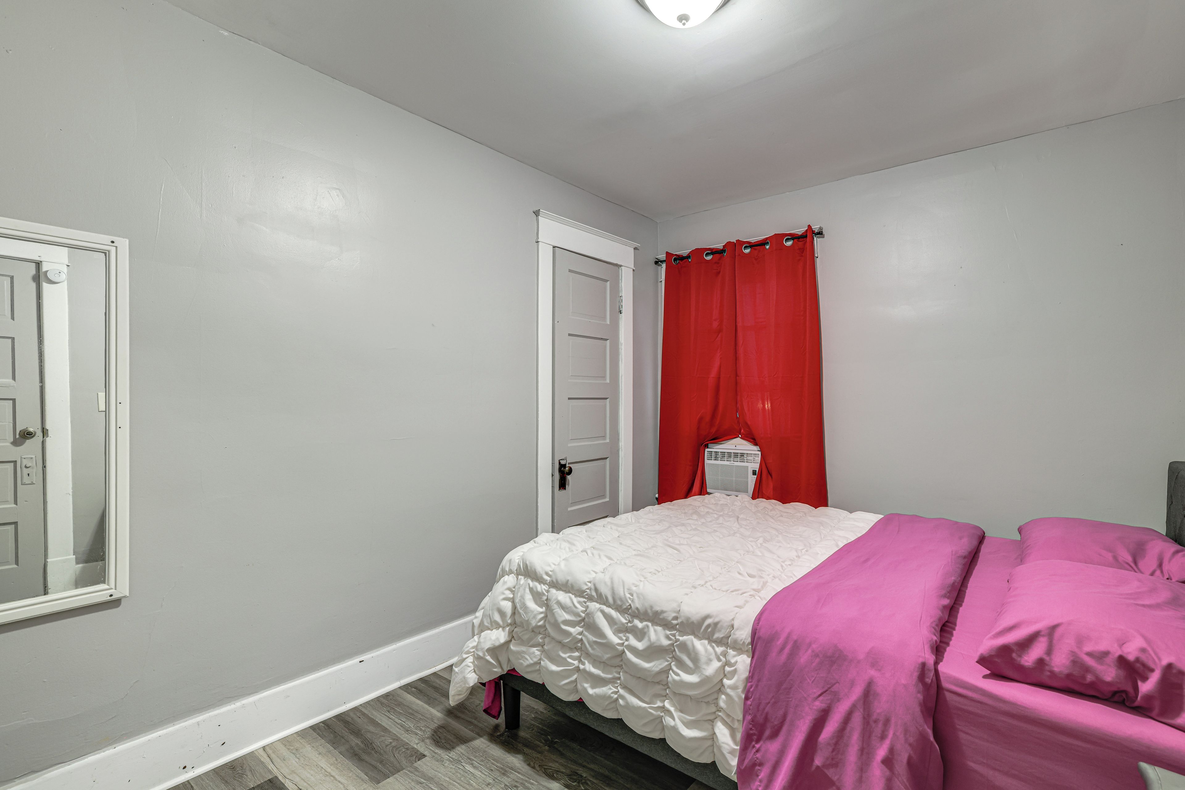 A bedroom with a bed, a door, and a window with red curtains.