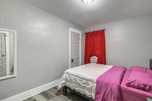 A bedroom with a bed, a door, and a window with red curtains.