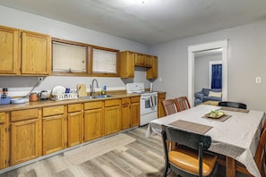 A compact kitchen with wooden cabinets, a white stove, and a dining area with a table and chairs.