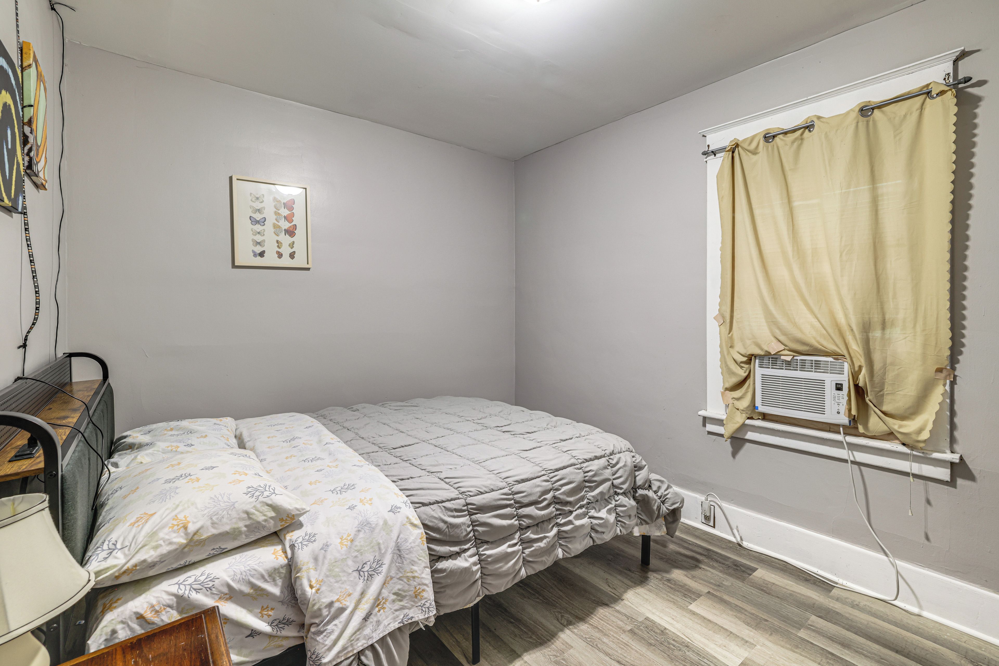 A bedroom with a bed, a desk, a radiator, and a window with curtains.