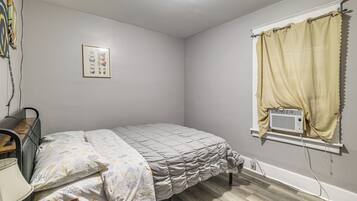Une chambre à coucher avec un lit, un bureau, un radiateur et une fenêtre avec des rideaux.