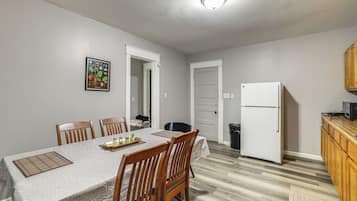 Un coin repas avec une table dressée pour quatre personnes, des chaises, un réfrigérateur et un buffet en bois.