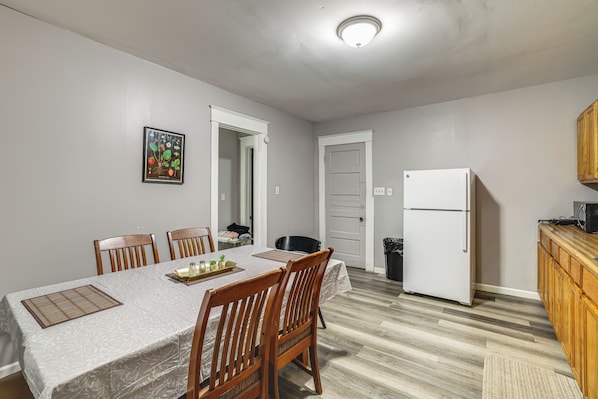 A dining area with a table set for four, chairs, a refrigerator, and a wooden cabinet.