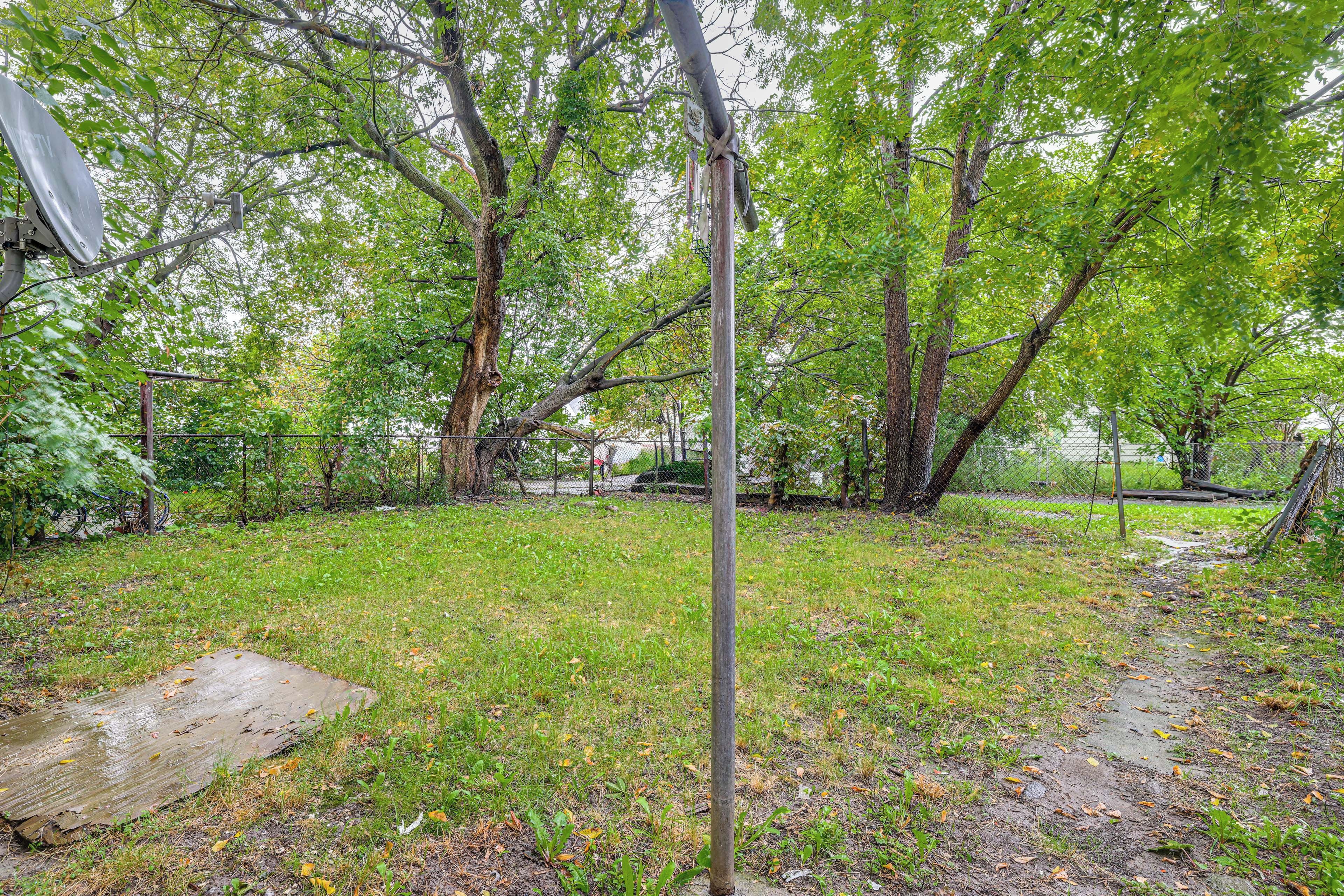 A fenced yard with trees, a metal pole, and a concrete slab.