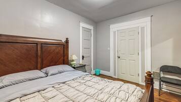 A bedroom with a wooden headboard, a bed with a beige quilt, a nightstand with a lamp, and a chair.
