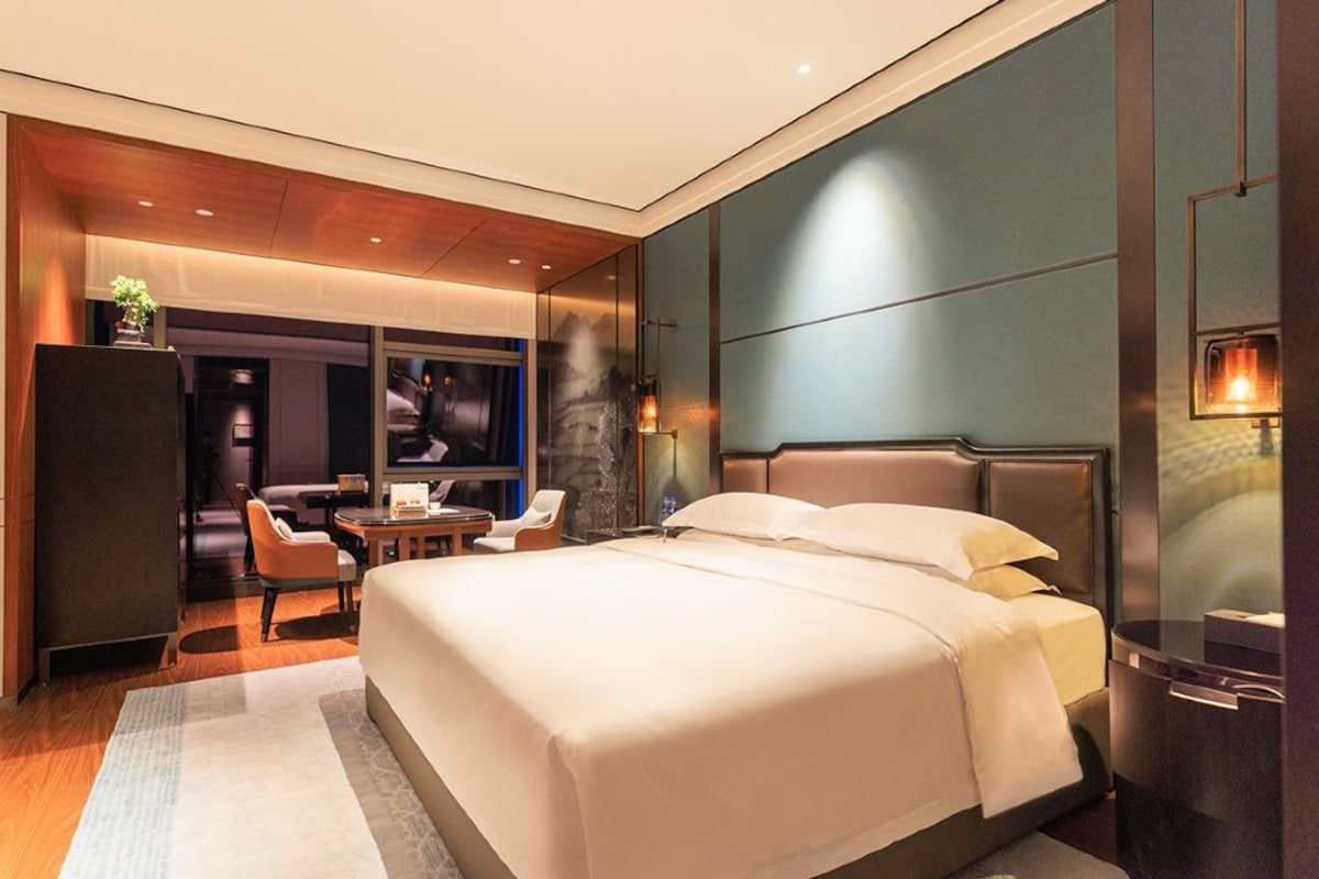 A modern hotel room with a large bed, a seating area with a table, and a television.