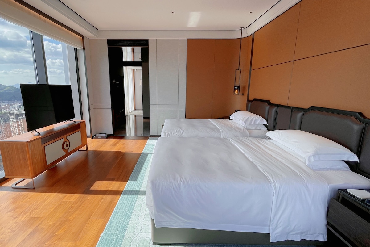 A hotel room with a large bed, a TV, and a view of the city.