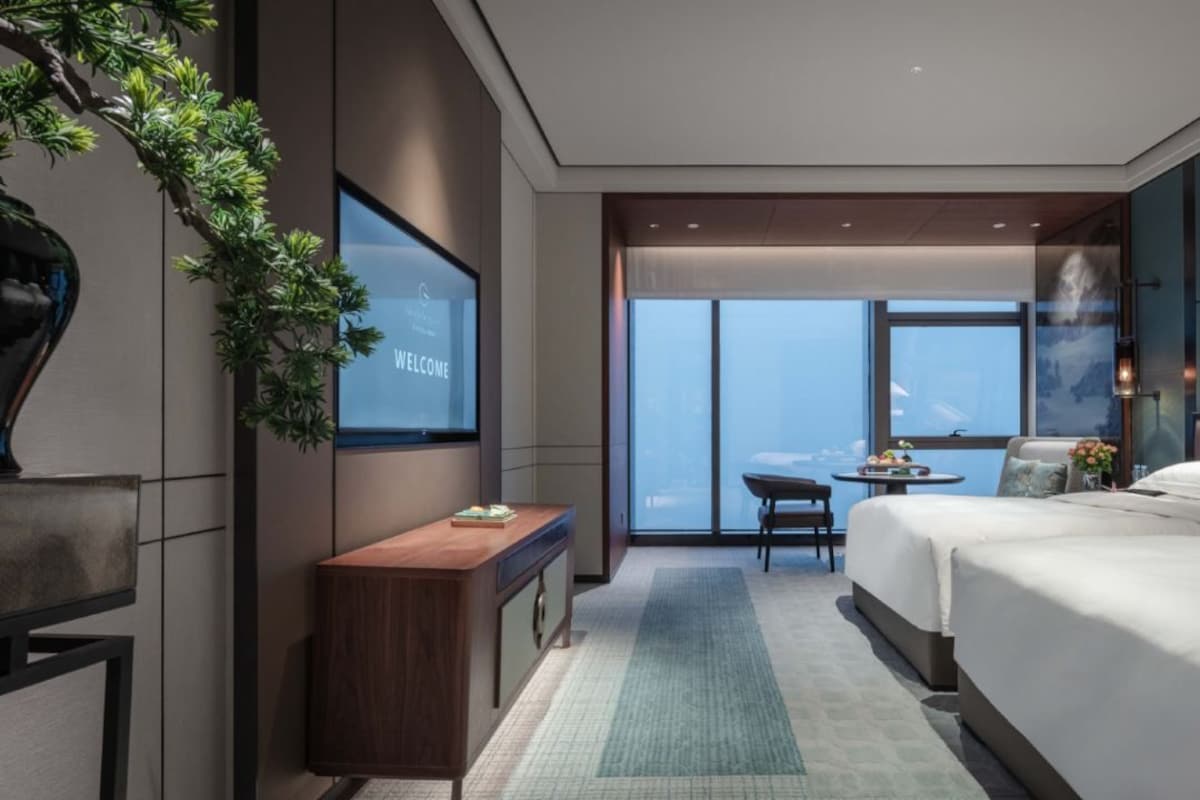 A modern hotel room with a large bed, a desk, a chair, and a television on the wall.