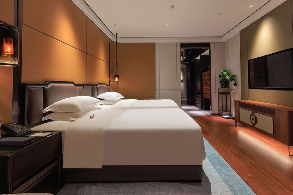 A modern hotel room with a large bed, bedside tables, a TV, and a wooden floor.