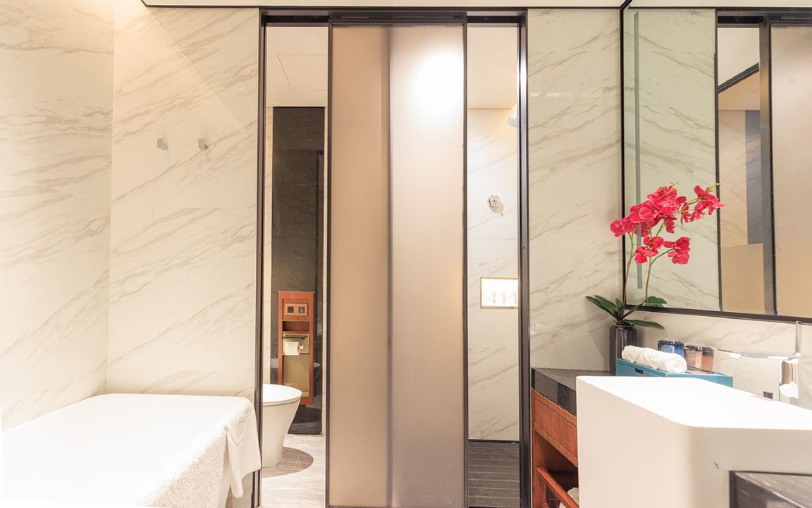 Een moderne badkamer met een marmeren wand, een wastafel, een spiegel en een toilet, zichtbaar door een schuifdeur.