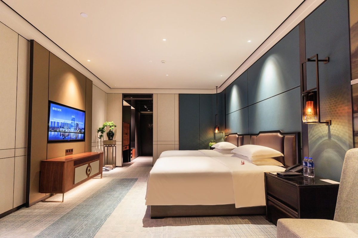 A modern hotel room with a large bed, a desk, a television, and a bathroom visible through an open door.