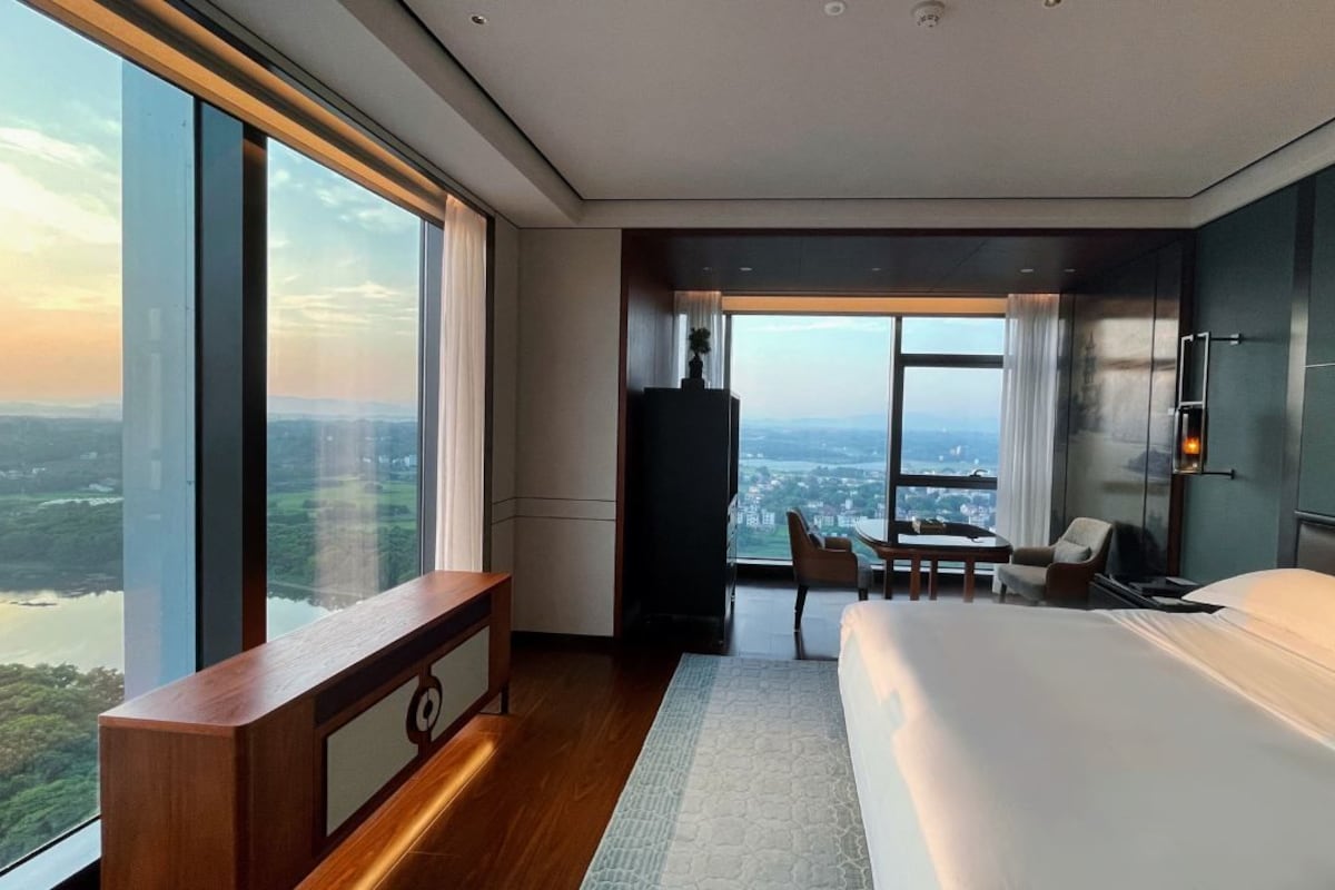 A modern hotel room with a large bed, a desk, and a view of a cityscape.