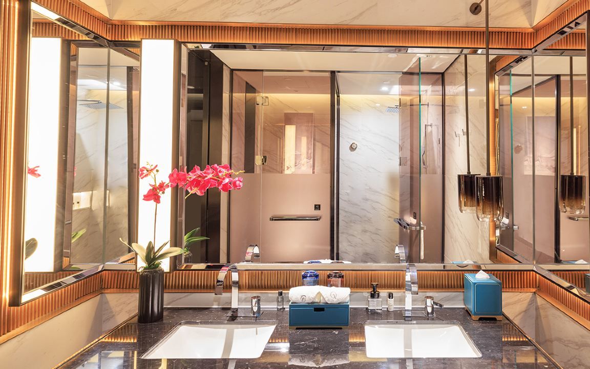 A modern bathroom with a large mirror, two sinks, a shower, and a potted plant.