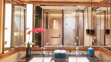 A modern bathroom with a large mirror, two sinks, a shower, and a potted plant.