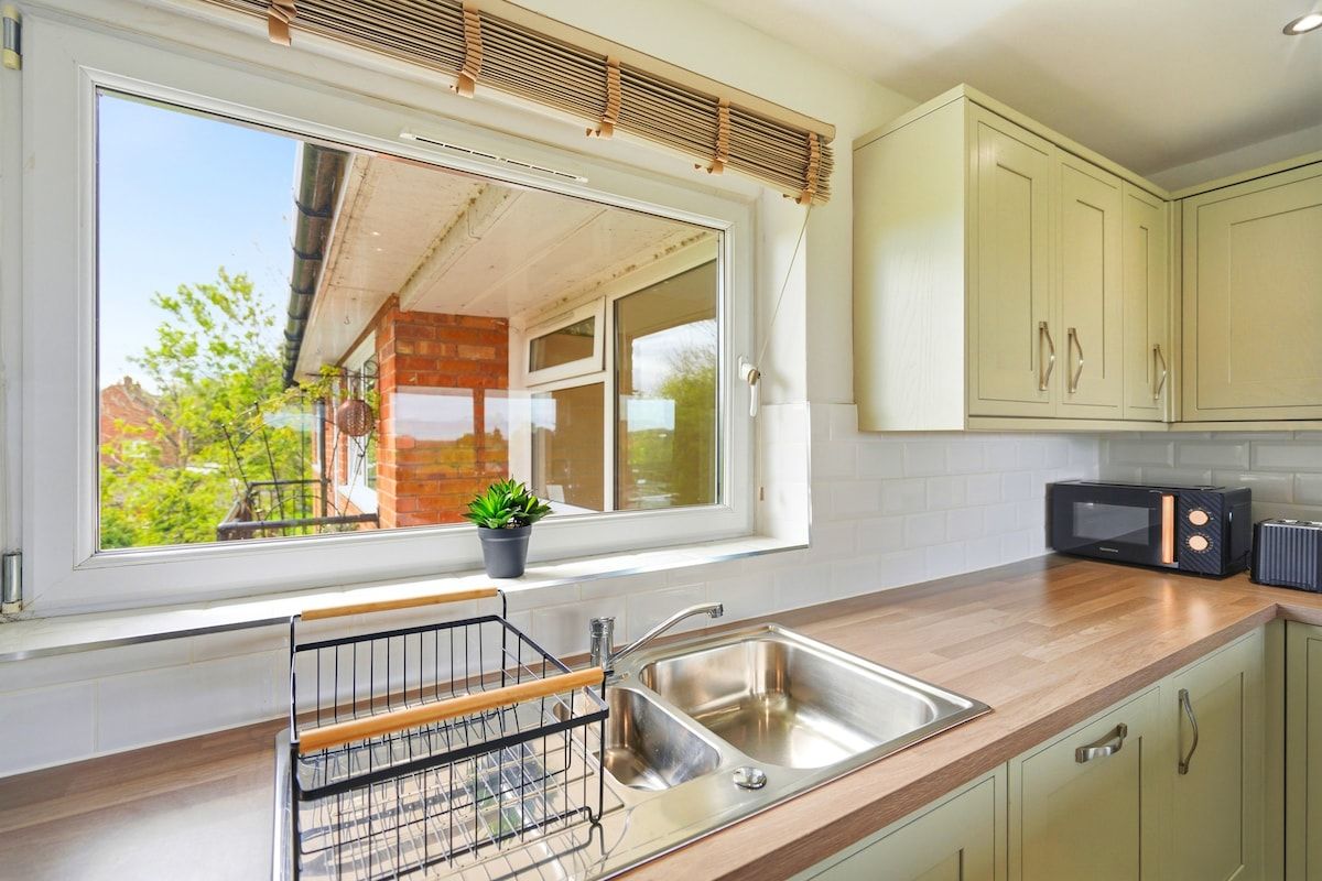 A kitchen with a large window, a sink, a microwave, and cabinets.