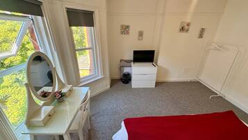 Een slaapkamer met een bed, een bureau met spiegel, een televisie en een radiator.