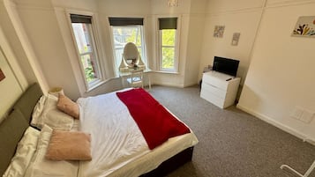 Een slaapkamer met een bed, een bureau, een stoel, een televisie en ramen.