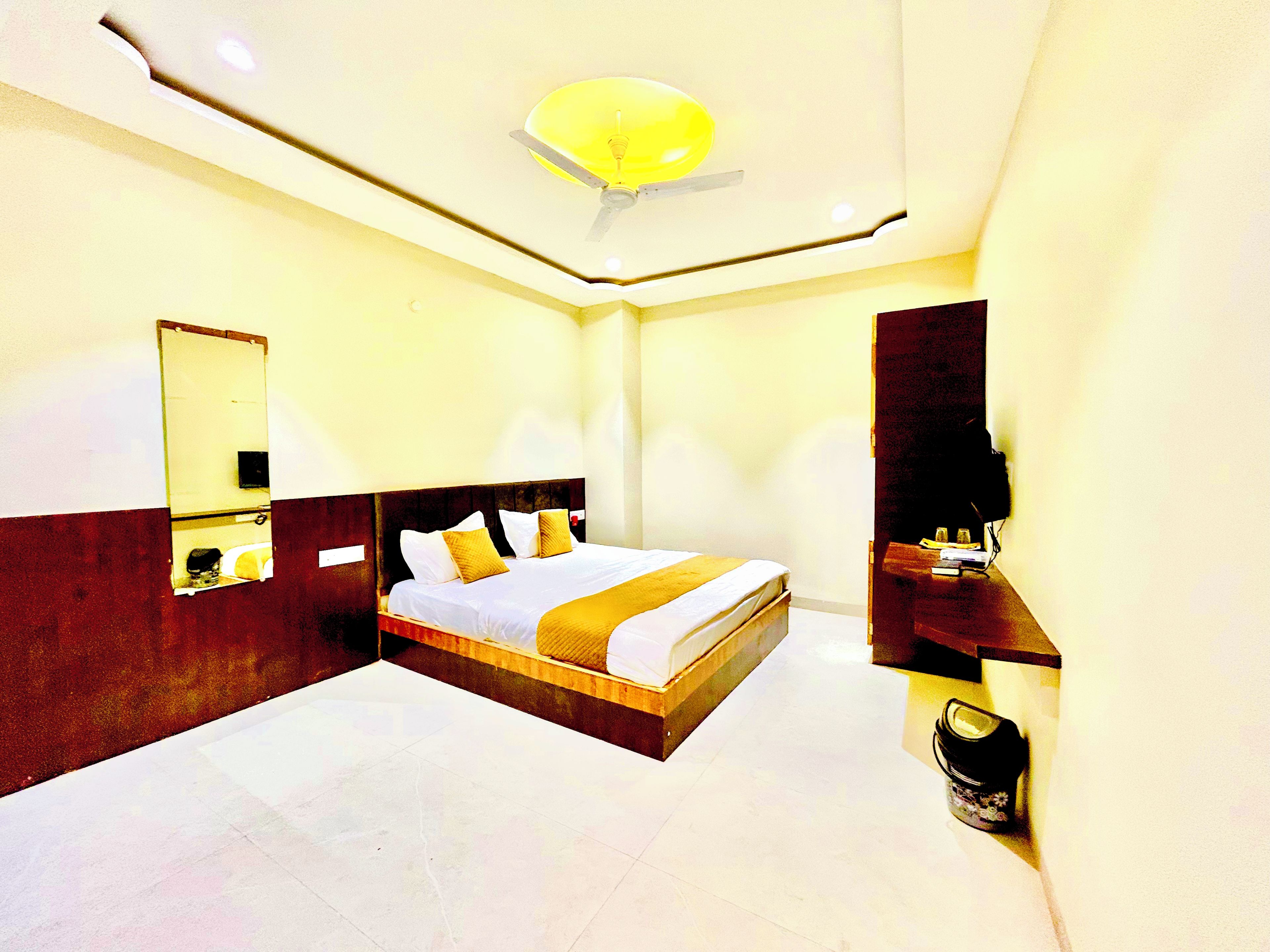 A hotel room with a large bed, a ceiling fan, a mirror, and a nightstand with a lamp.