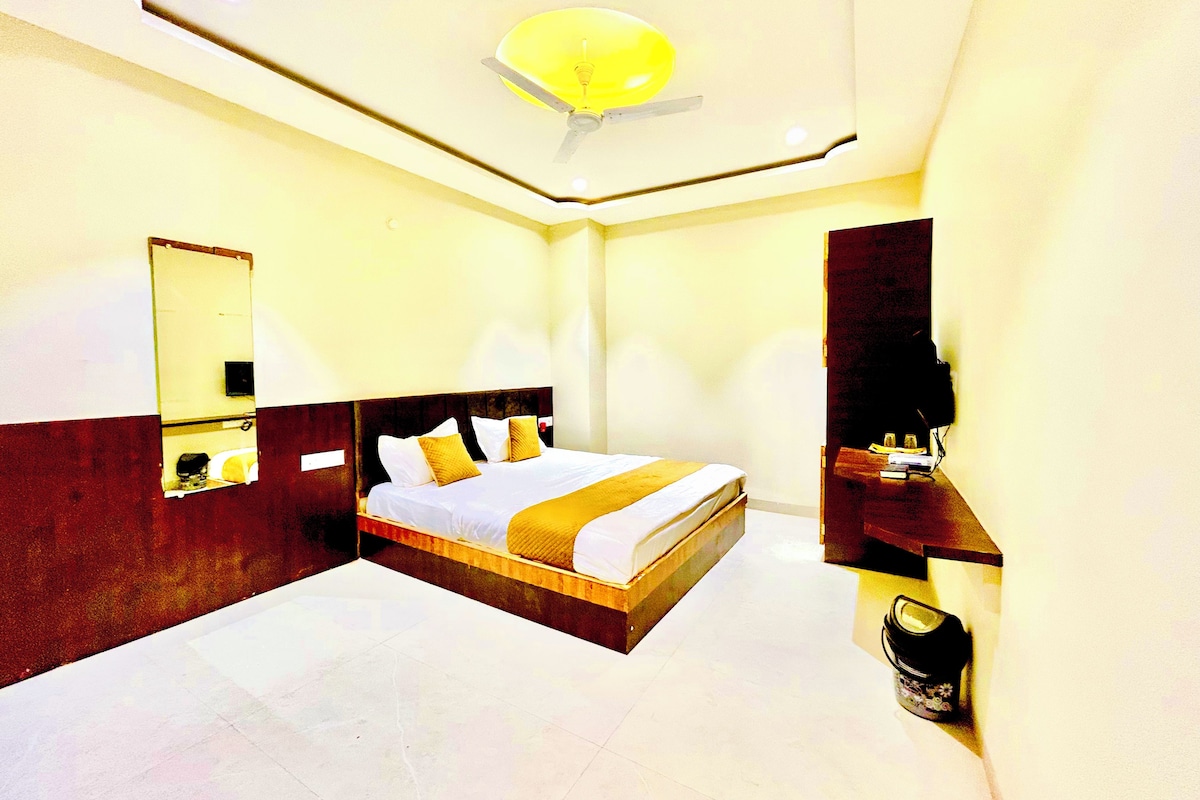 Habitación de hotel con una cama grande, un ventilador de techo, un espejo y una mesita de noche con lámpara.