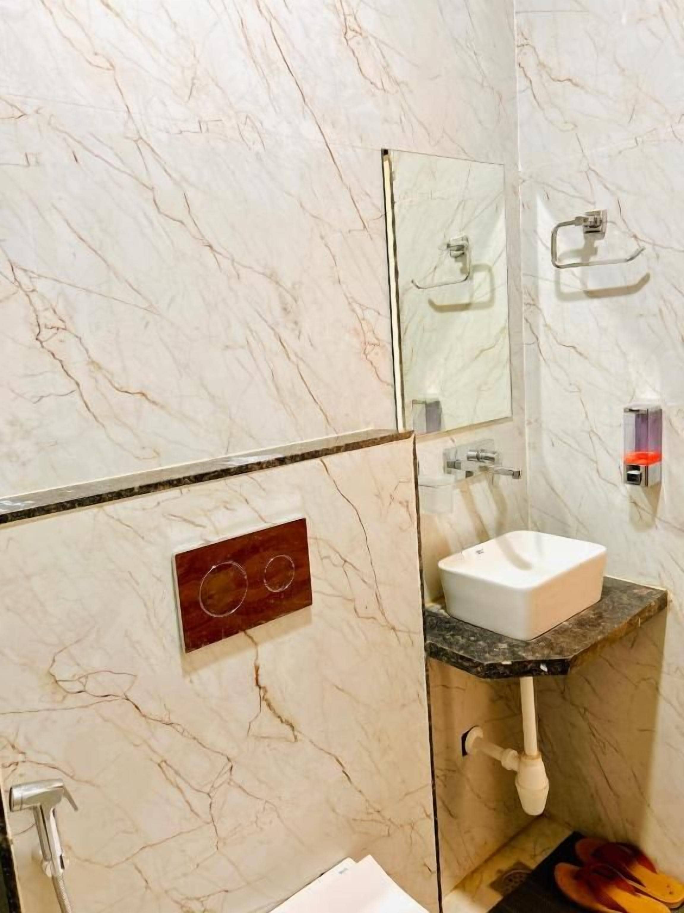 A bathroom with a marble wall, a sink, a mirror, and a towel rack.