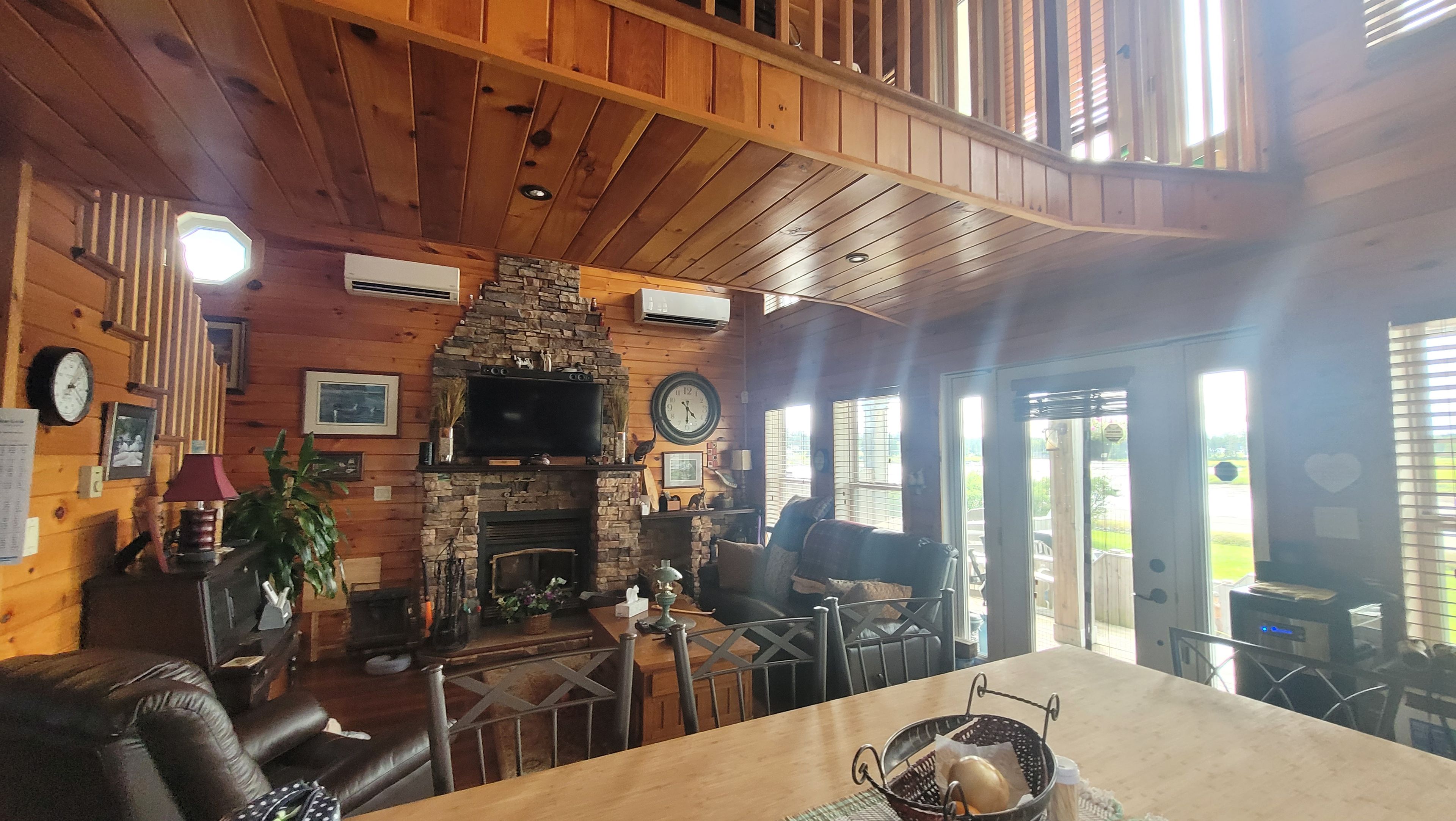 A cozy cabin interior with a stone fireplace, wooden ceiling, and a dining area with a table and chairs.