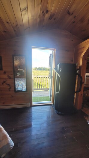 Interior de una cabaña de madera con una puerta que da a una terraza exterior.