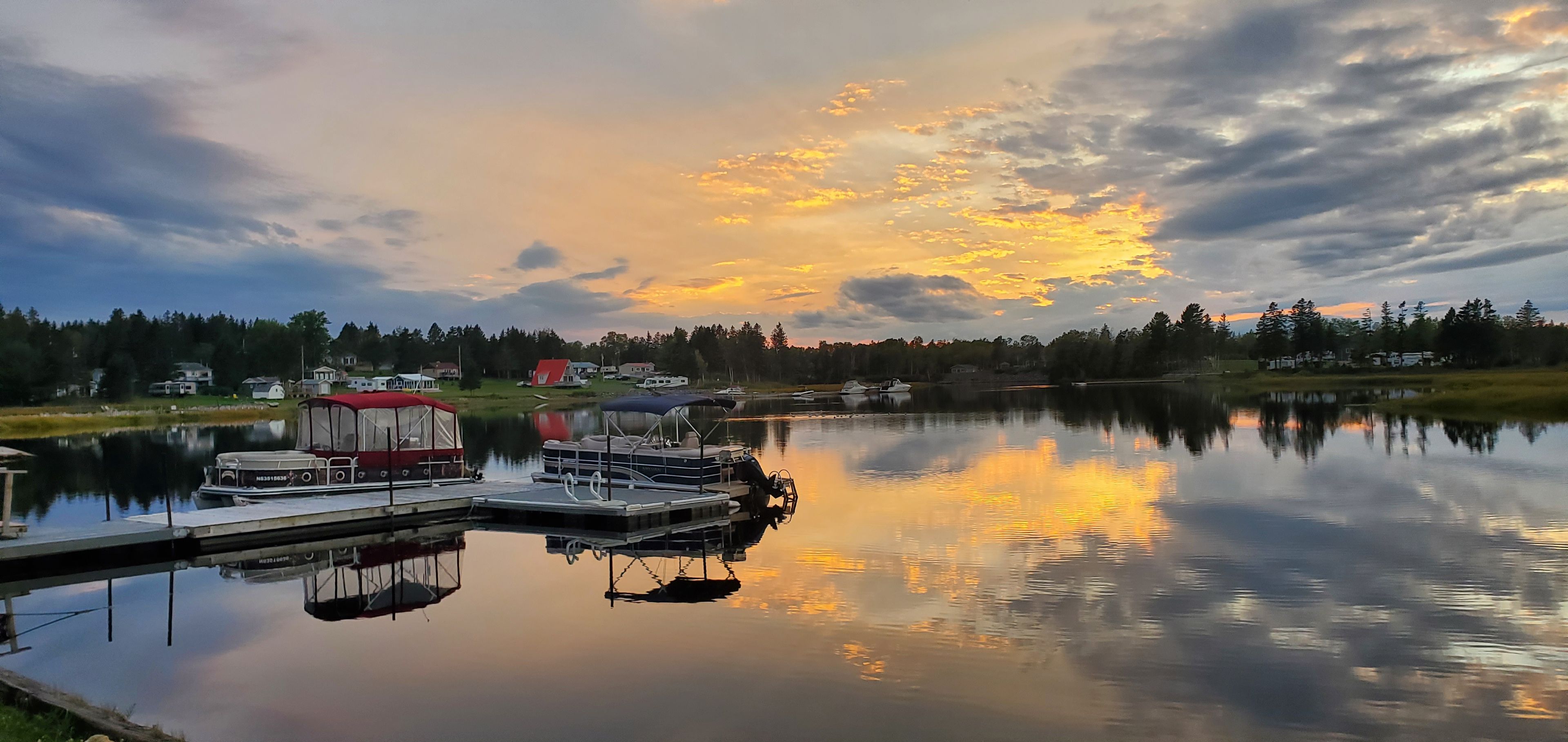 A calm lake with boats docked, surrounded by trees and houses.
