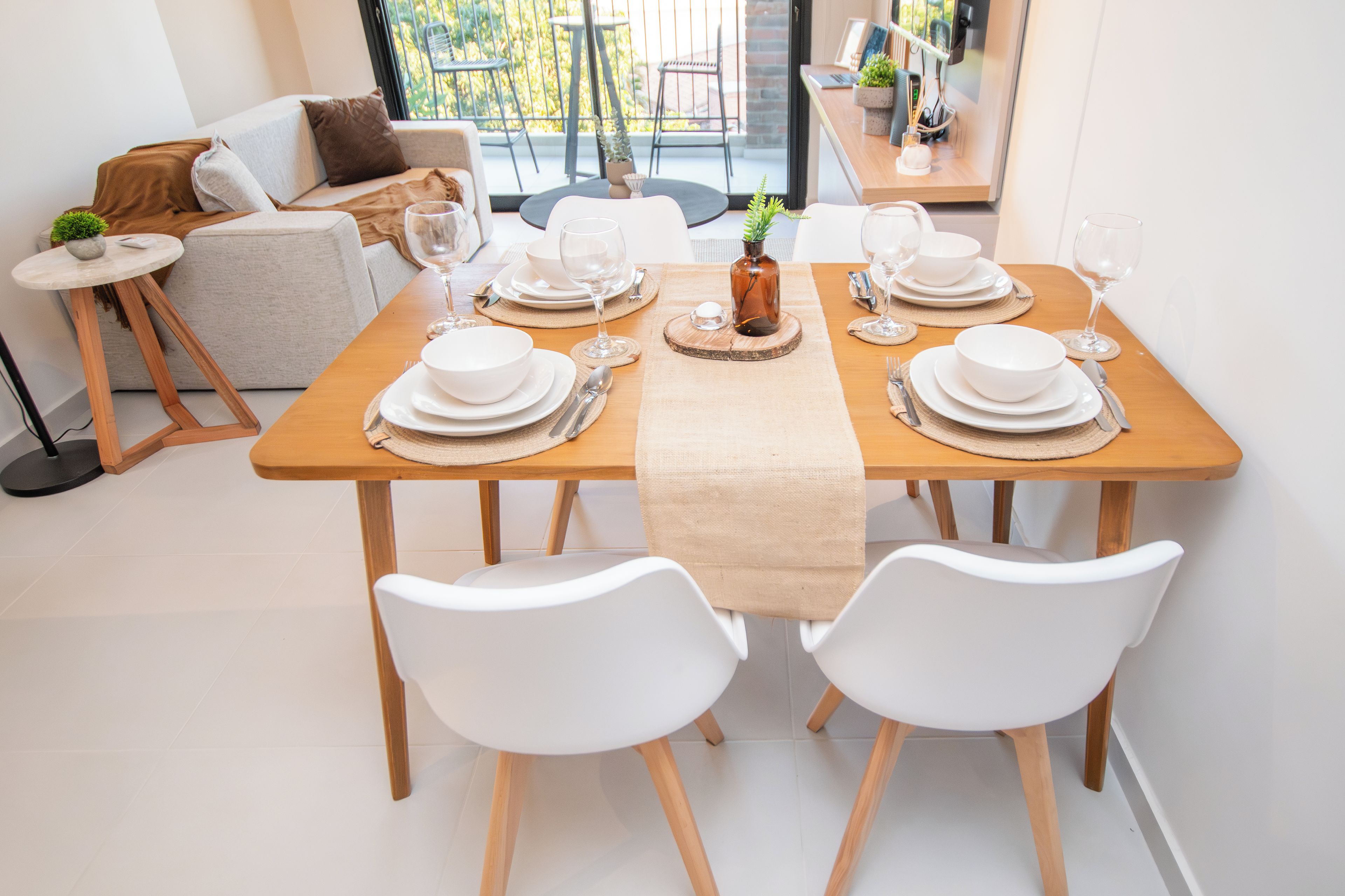 Une table à manger dressée avec de l’argenterie, de la vaisselle blanche et des verres, entourée de chaises blanches.