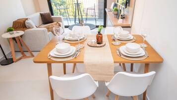 Une table à manger dressée avec de l’argenterie, de la vaisselle blanche et des verres, entourée de chaises blanches.