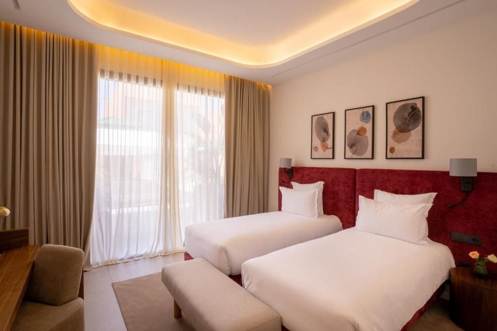 A hotel room with two beds, a desk, a chair, and a large window with curtains.