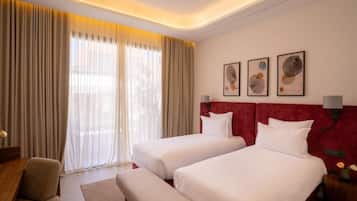 A hotel room with two beds, a desk, a chair, and a large window with curtains.