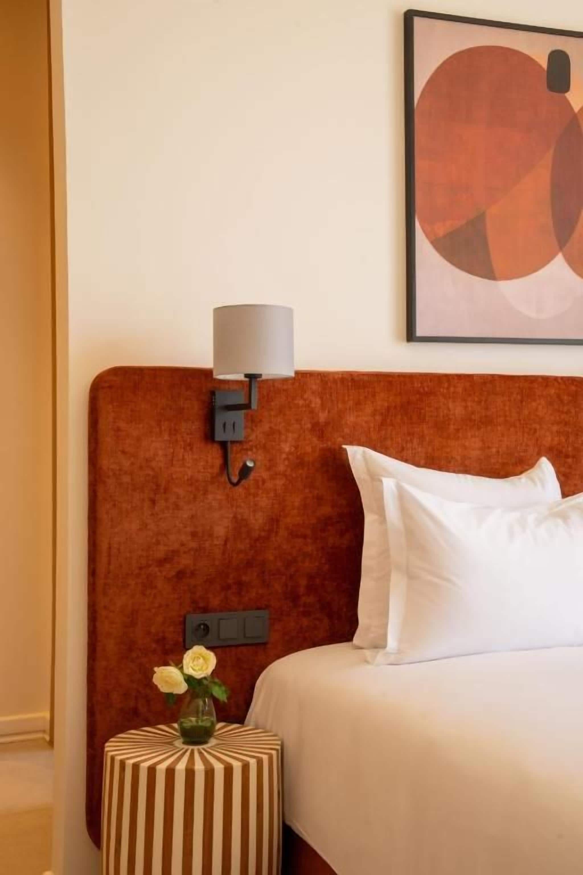Hotellihuone, jossa on sänky, yöpöytä lampun kanssa ja seinään asennettu valokytkin.
