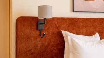 Hotellihuone, jossa on sänky, yöpöytä lampun kanssa ja seinään asennettu valokytkin.