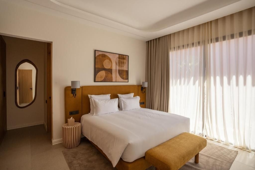 A hotel room with a large bed, a bedside table, a mirror, and a window with curtains.