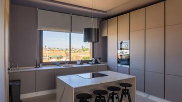 Een moderne keuken met een groot raam, een centraal kookeiland en barstoelen.