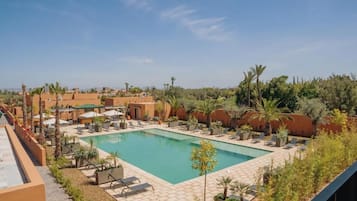 A swimming pool with lounge chairs and umbrellas, surrounded by greenery and buildings.