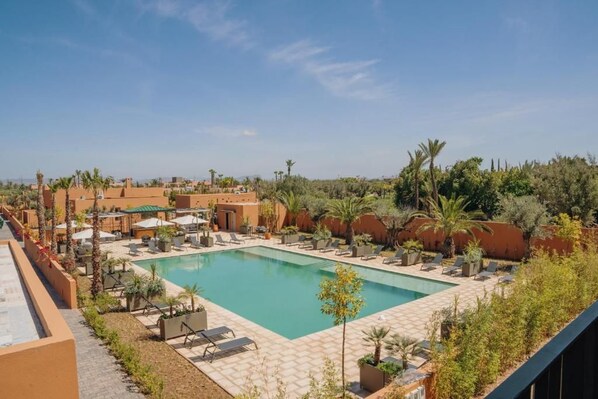 A swimming pool with lounge chairs and umbrellas, surrounded by greenery and buildings.