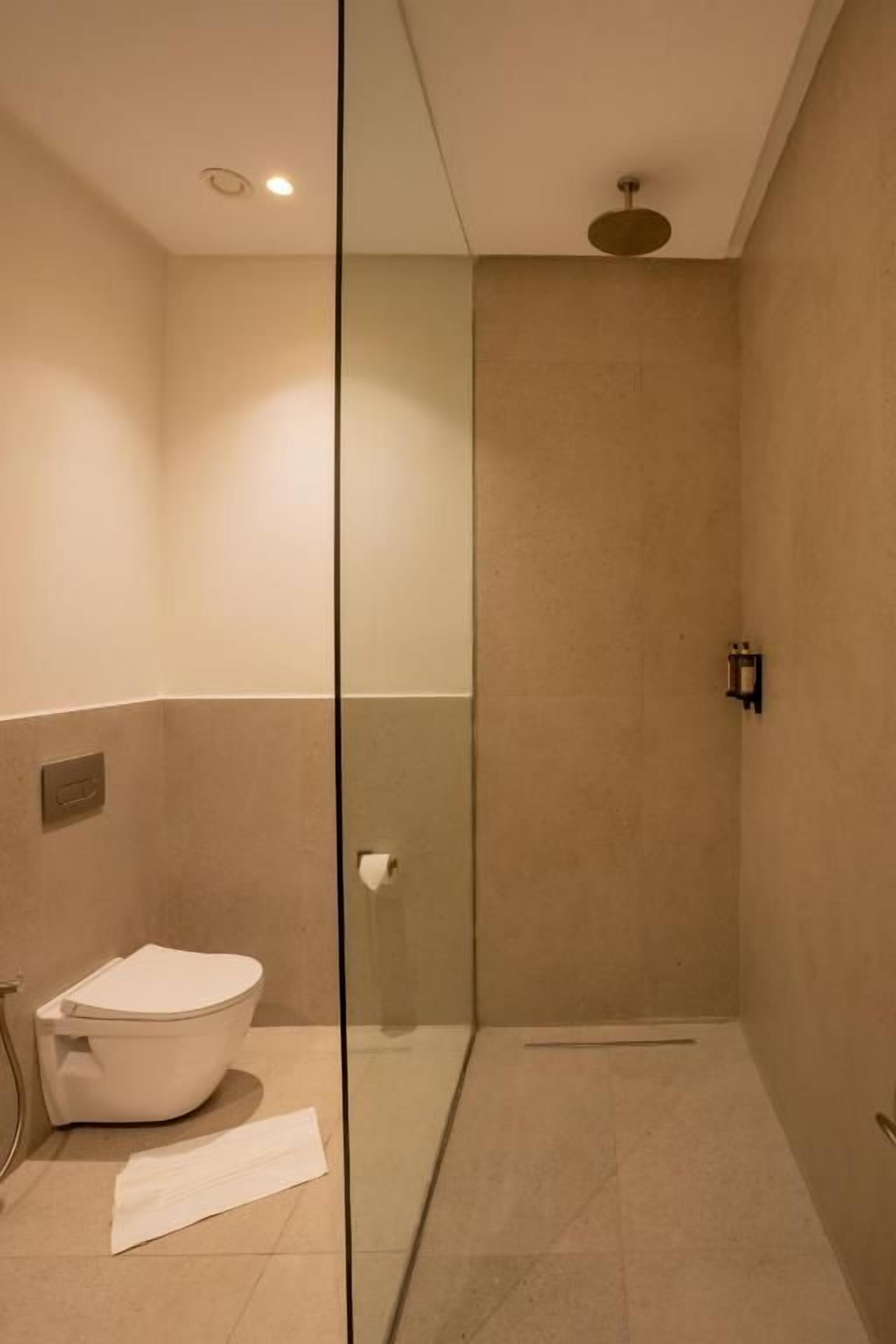 A bathroom with a toilet, a glass shower enclosure, and a towel on the floor.