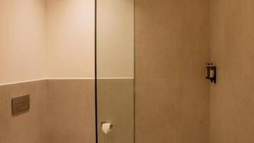 A bathroom with a toilet, a glass shower enclosure, and a towel on the floor.