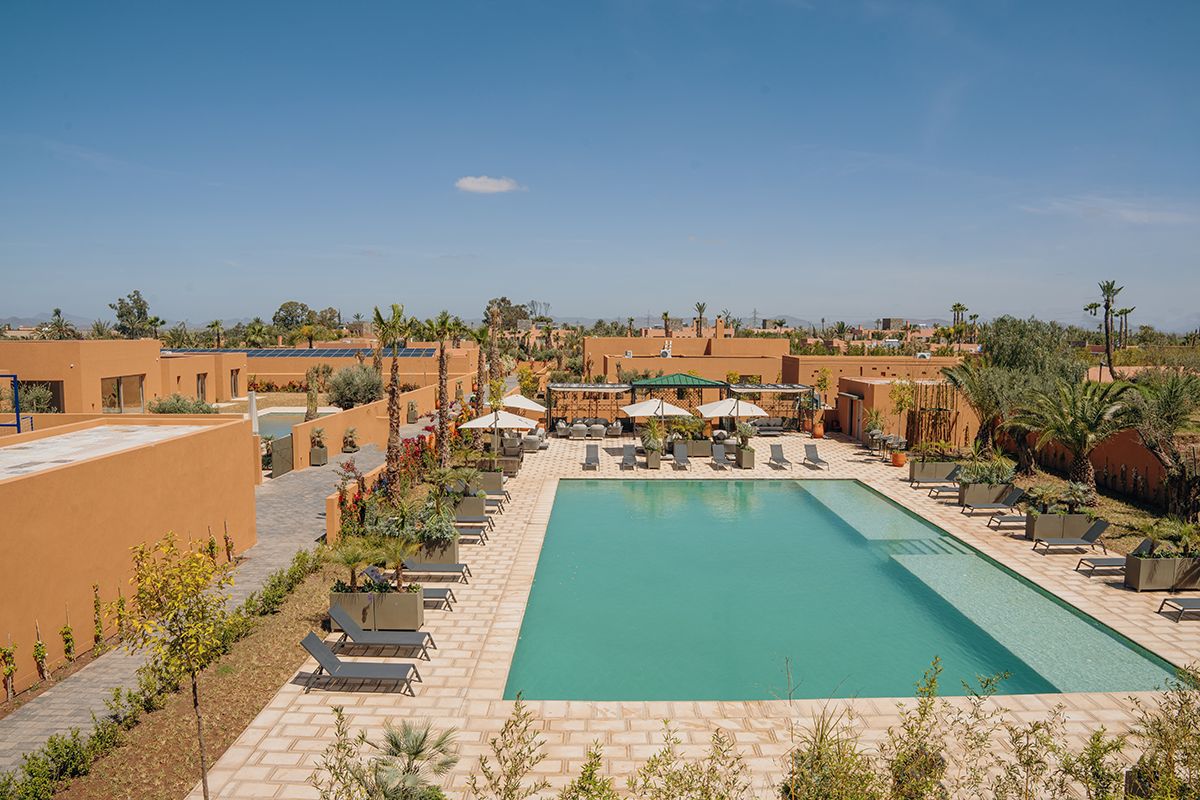 A pool area with lounge chairs and umbrellas, surrounded by buildings with a desert landscape in the background.