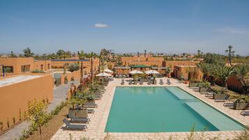 A pool area with lounge chairs and umbrellas, surrounded by buildings with a desert landscape in the background.