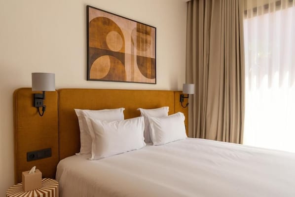 A hotel room with a large bed, two bedside lamps, a wall-mounted artwork, and a window with curtains.