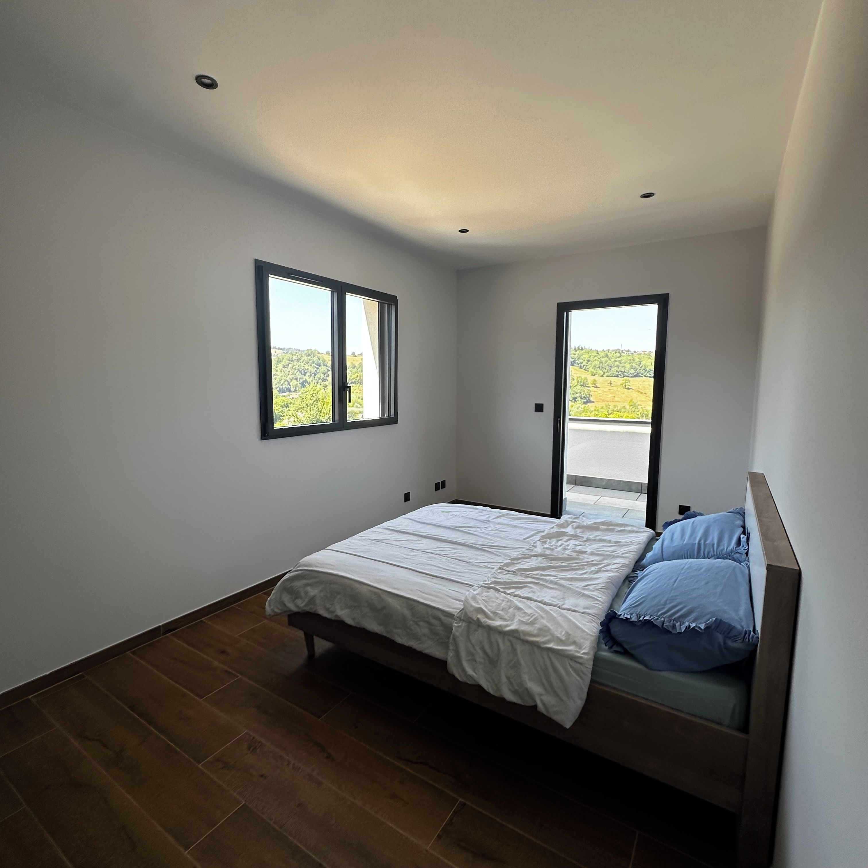 Une chambre à coucher avec un lit, deux fenêtres et une vue sur un paysage verdoyant.