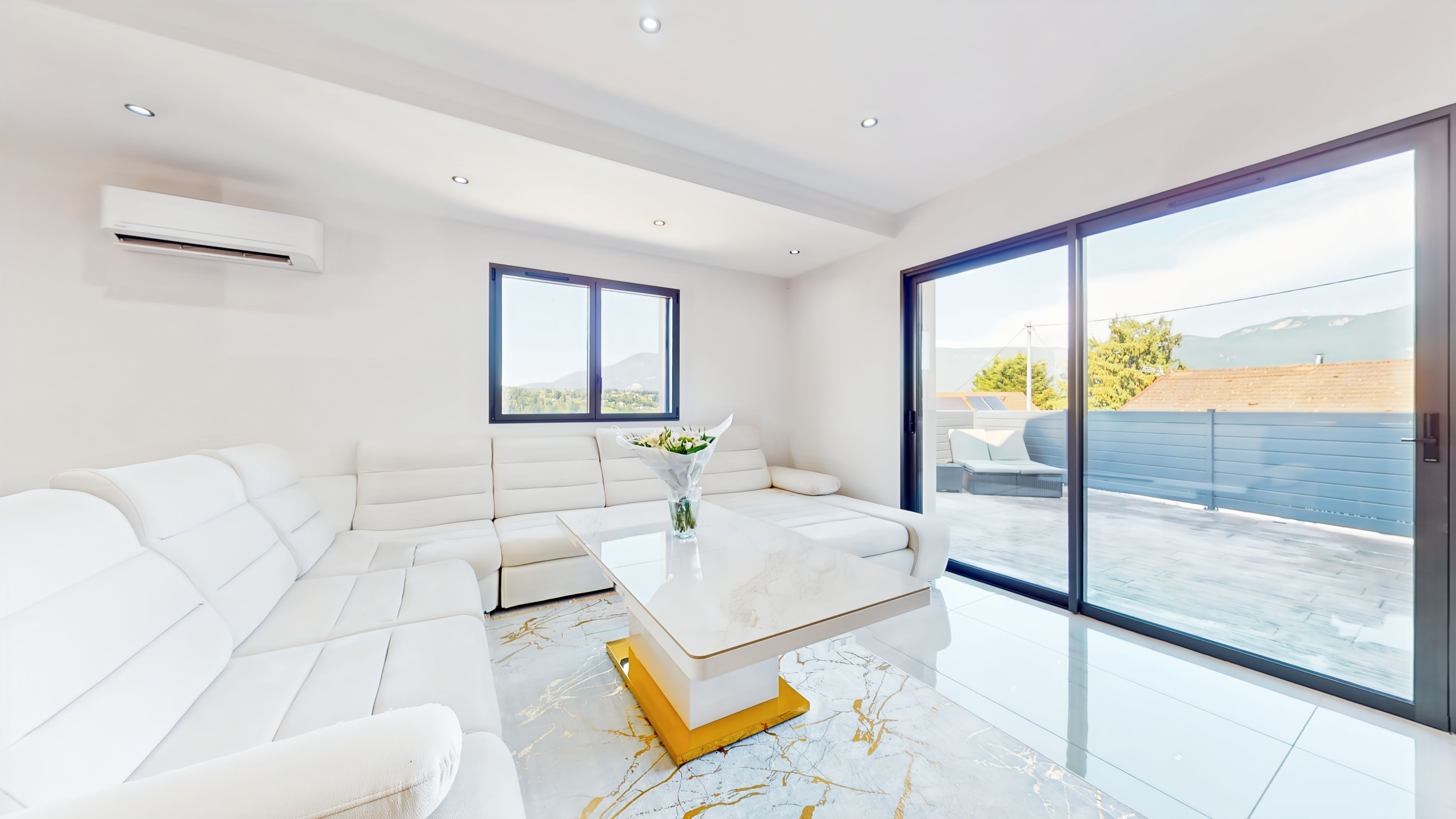 Uma sala de estar moderna com um sofá seccional branco, uma mesa de centro de mármore e vista para o exterior através de grandes portas de correr de vidro.