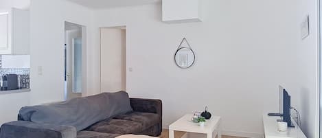 Un salon moderne avec un canapé gris, une petite table d’appoint blanche, un meuble blanc et un luminaire fixé au mur.