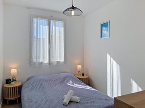 Ein Schlafzimmer mit einem Bett, zwei Nachttischlampen, einem Fenster mit Vorhängen, einer Deckenleuchte und einem kleinen Bild an der Wand.