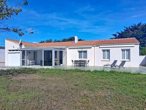 Ein zweistöckiges Haus mit Ziegeldach, überdachter Terrasse und Rasen.