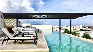 Una piscina a sfioro sul tetto con poltroncine e vista sulla città.